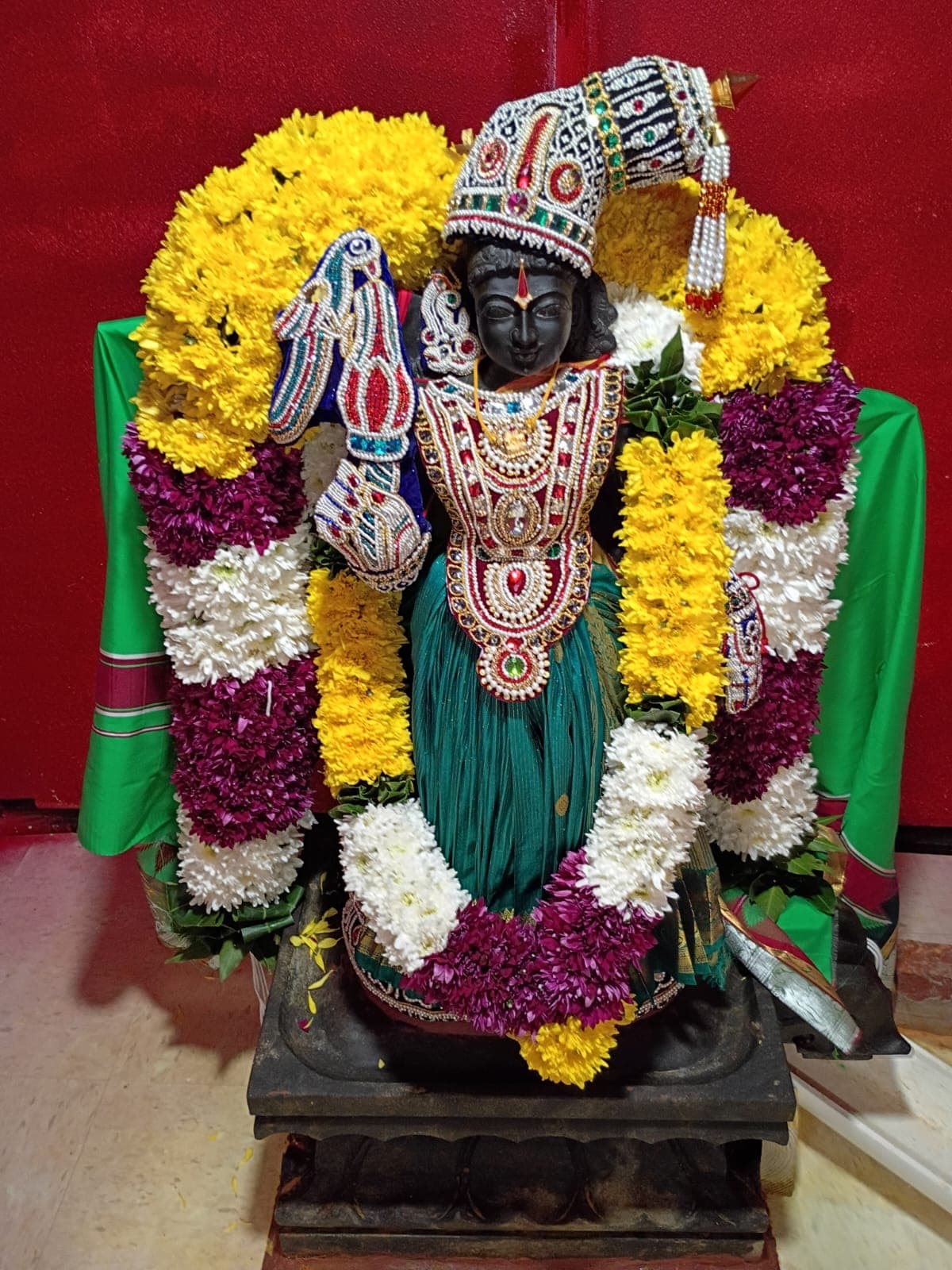 Goddess Sri Andal standing in the shrine, wearing a green sari, pearl crown, and yellow and purple flower garlands