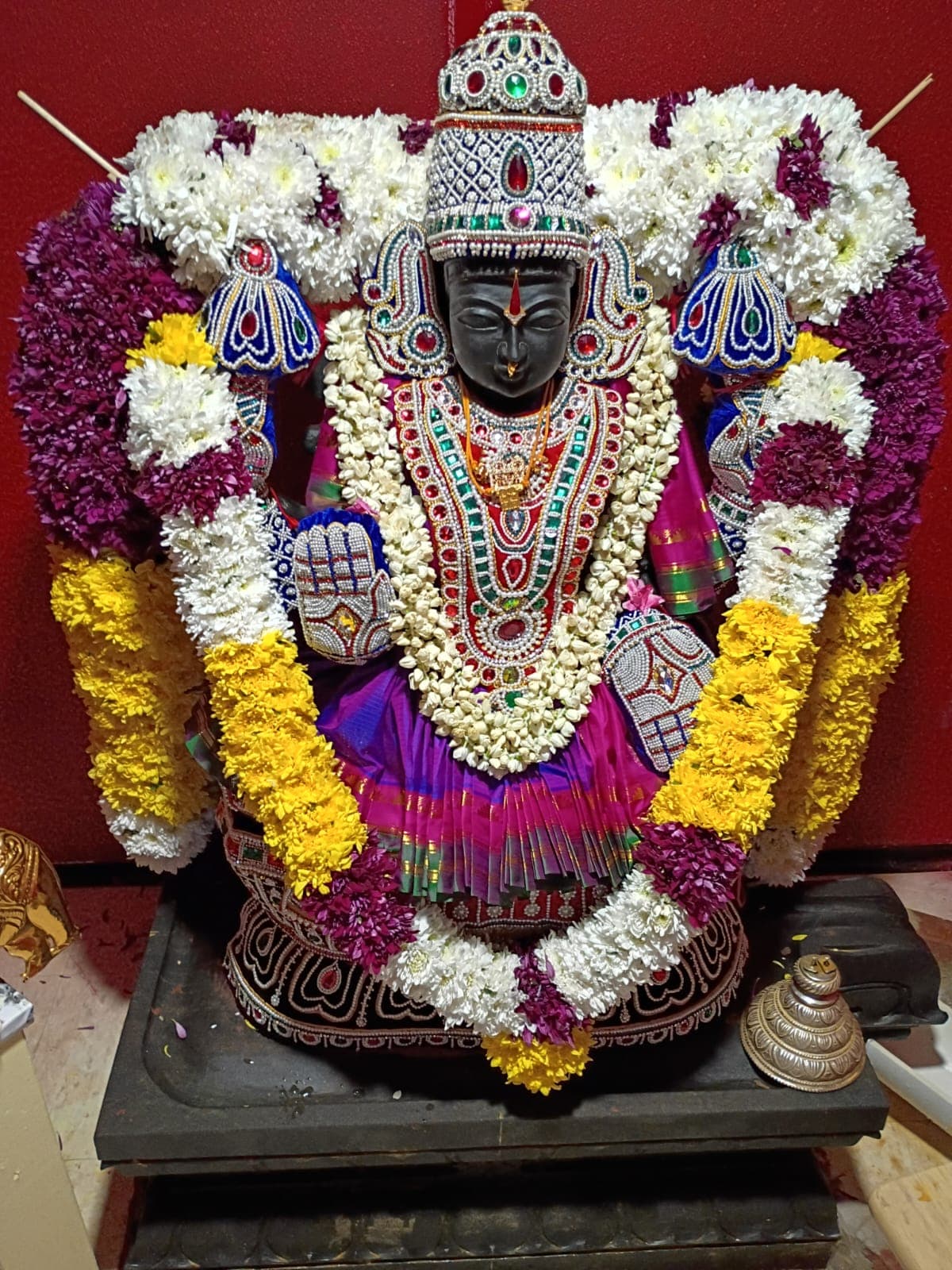 Goddess Sri Mahalakshmi seated in the shrine, wearing a magenta sari, pearl crown, and flower garlands